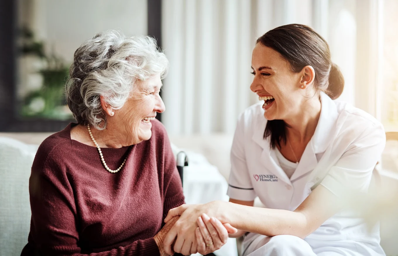 An older woman and her caregiver sitting together at home, relaxed and at ease